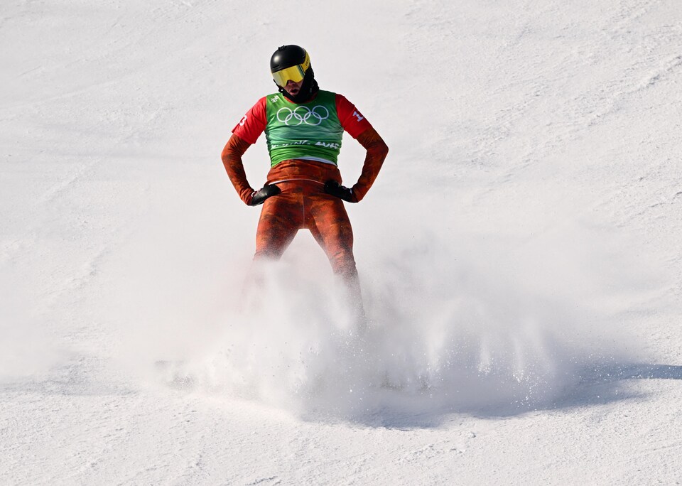 Un athlète debout sur sa planche, vu de face les deux mains sur les hanches, ses jambes cachées par la neige après un freinage.