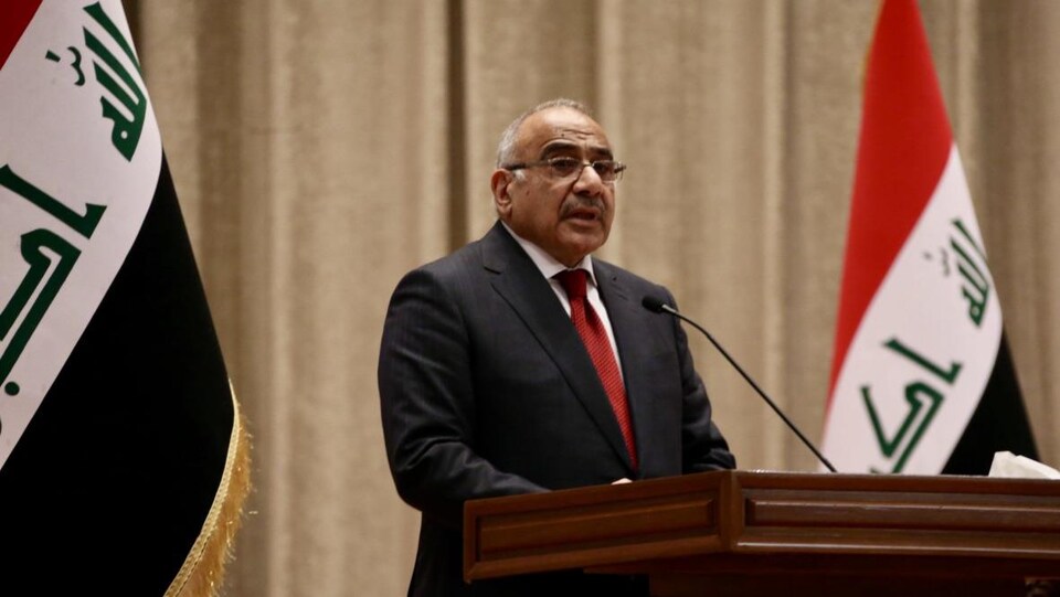 Adel Abdel Mahdi parle sur un podium, entouré de deux drapeaux irakiens.
