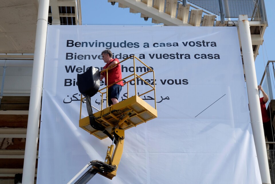 Un volontaire de la Croix-Rouge installe une immense affiche où il est inscrit, dans plusieurs langues différentes, « Bienvenue chez vous ».