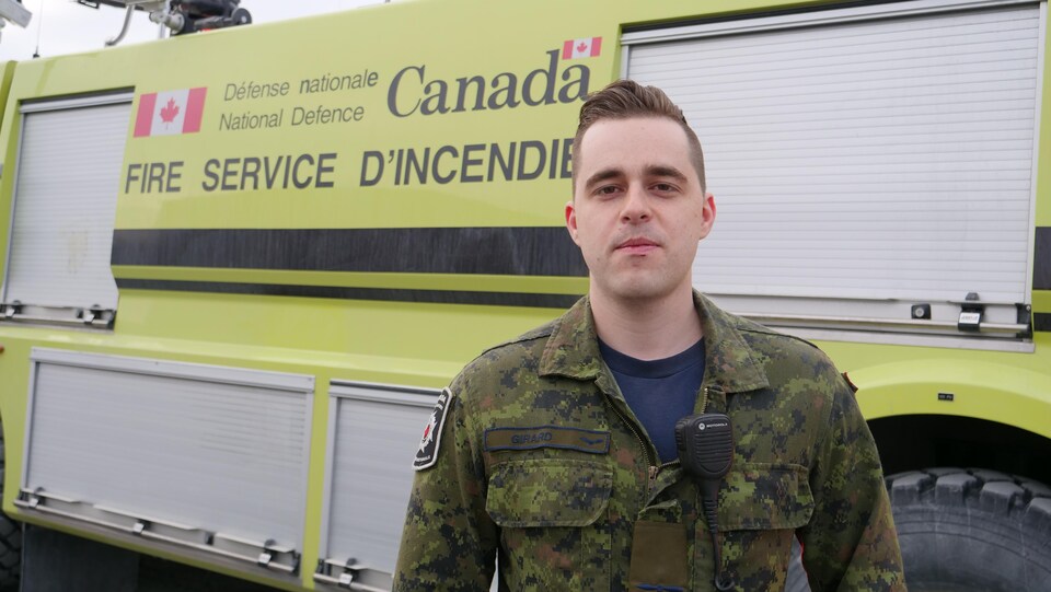 Un homme en uniforme de l'armée devant un camion de pompier. 