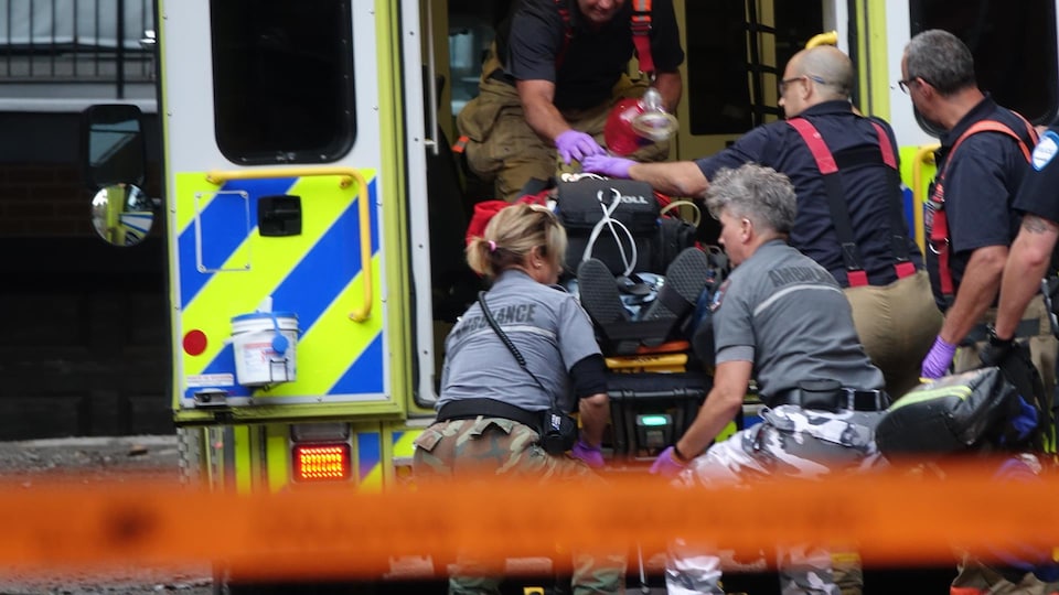 Des ambulanciers montent le corps de l'homme, qui est sur une civière, dans l'ambulance.