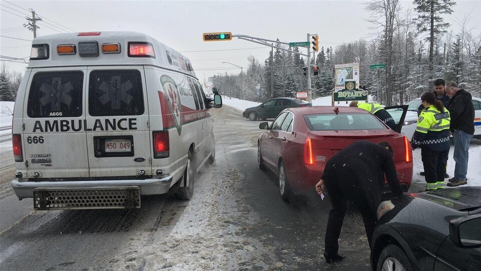 Une ambulance, en hiver, est arrêtée près d'une voiture rouge.