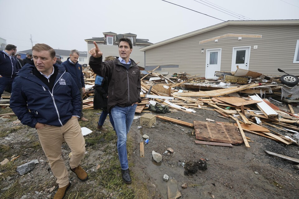 Andrew Furey et Justin Trudeau marchent le long de maisons endommagées.
