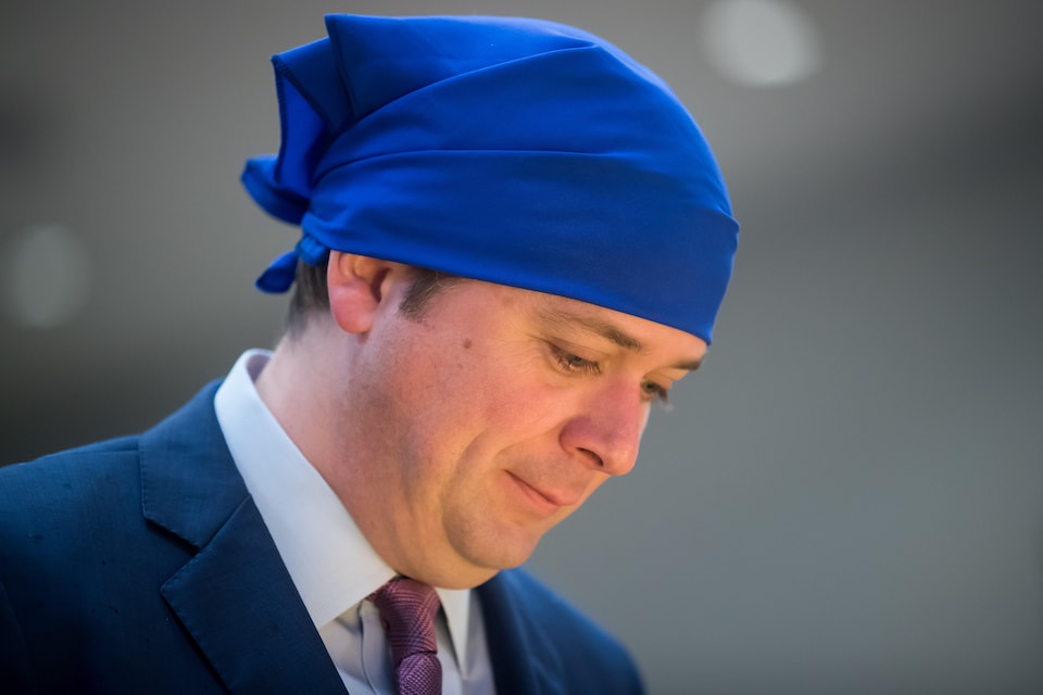 Un homme portant un complet avec une cravate porte également un foulard bleu traditionnel sur sa tête.