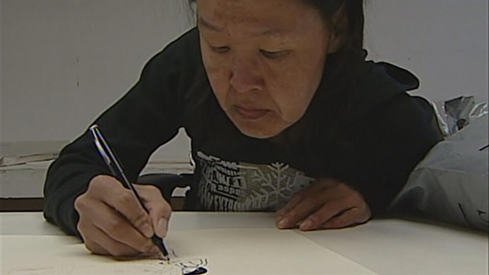 Annie Pootoogook est en train de dessiner avec un crayon noir sur une feuille blanche.