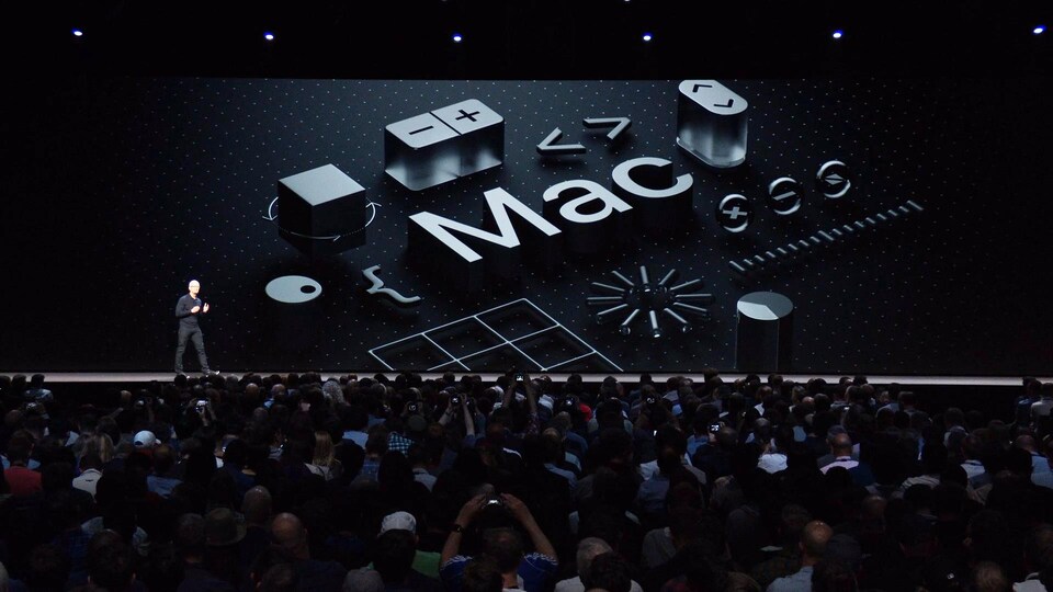 Une capture d'écran de la présentation d'Apple montrant Tim Cook sur la scène d'un amphithéâtre avec le mot « Mac » affiché à l'écran derrière lui.
