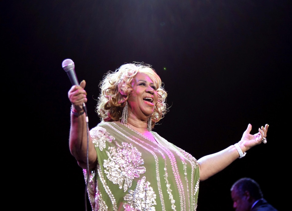 Aretha Franklin écarte les bras, alors qu'elle tient le micro dans sa main droite, et chante, lors d'un concert à New York, en 2012.