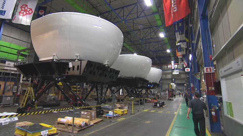 On voit de gros simulateurs blancs, qui ont la forme de coupoles, alignés sur des plates-formes dans une usine de CAE.