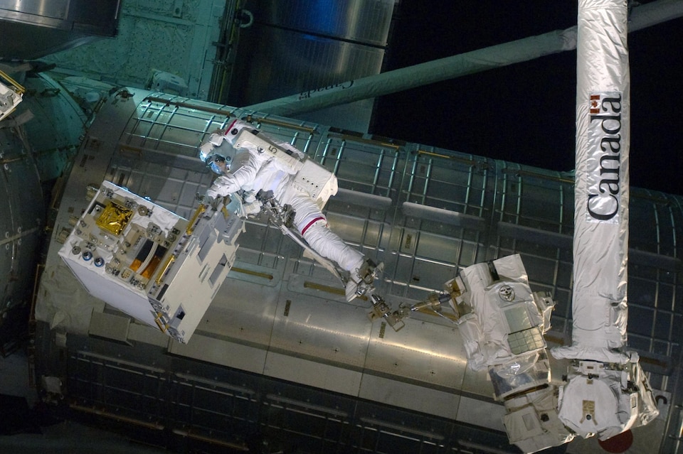 Un astronaute flotte dans l'espace et tente de réparer un appareil. 