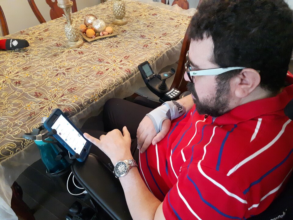 Assis dans un fauteuil roulant, un homme utilise son téléphone mobile.