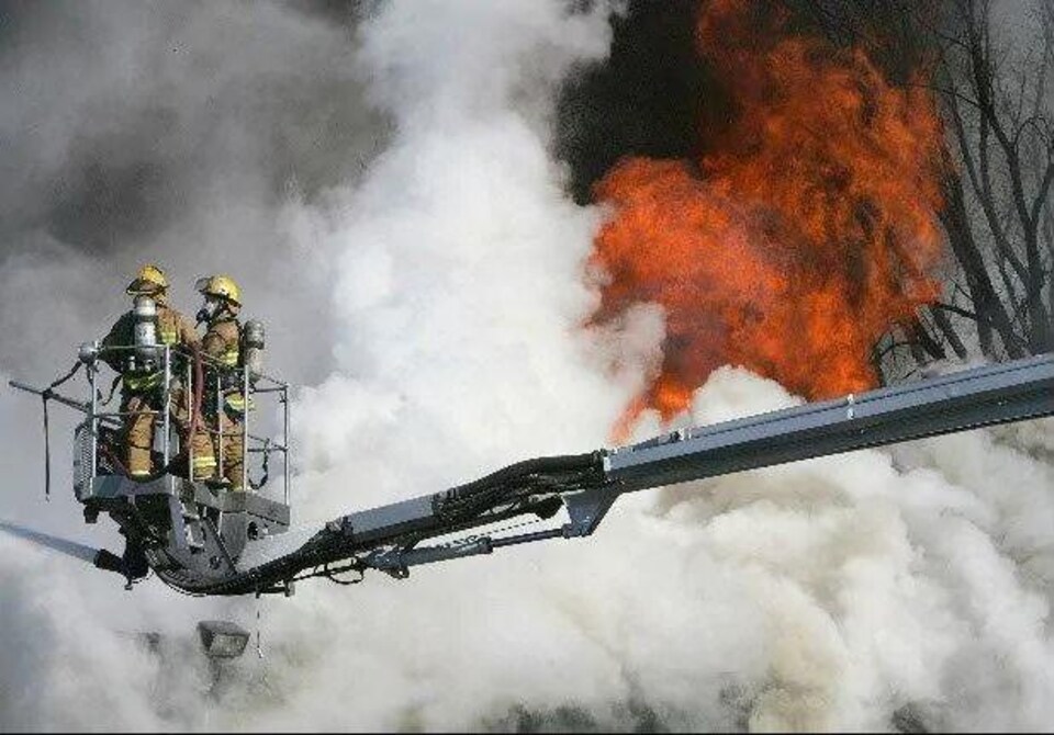 Le pompier manie une lance d'incendie du haut d'une plateforme près des flammes