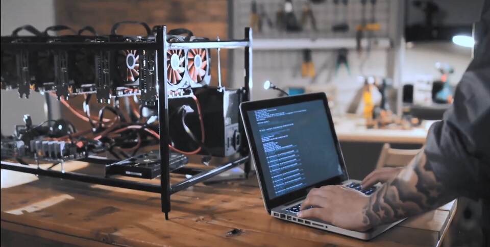 Quelqu'un utilise un ordinateur portable déposé sur une table en bois devant une machine composée de ventilateurs pour ordinateur et de fils électriques.
