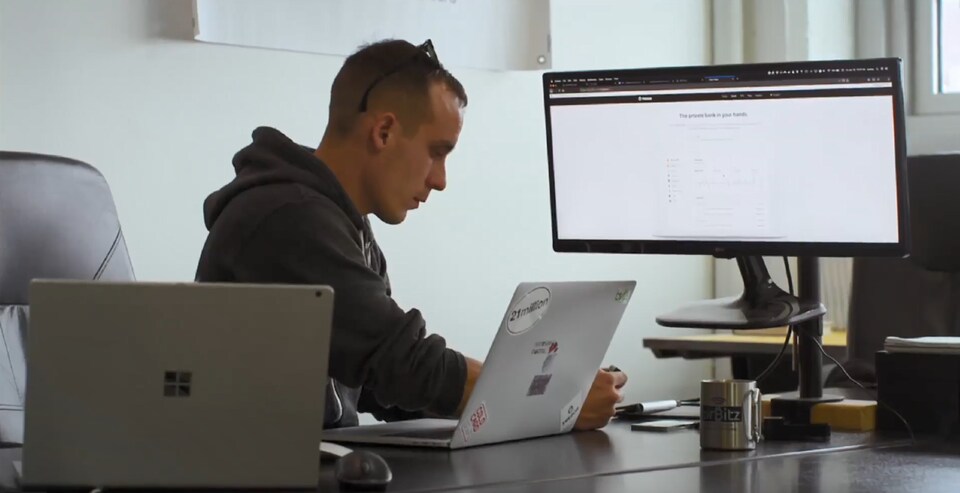 Un homme avec des lunettes sur la tête travaille à un bureau avec trois ordinateurs différents.