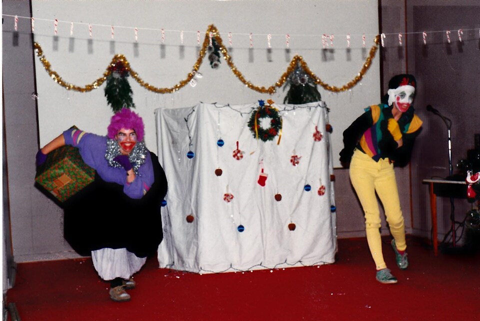 Deux personnes déguisées en clown avec un gros cadeau derrière eux.