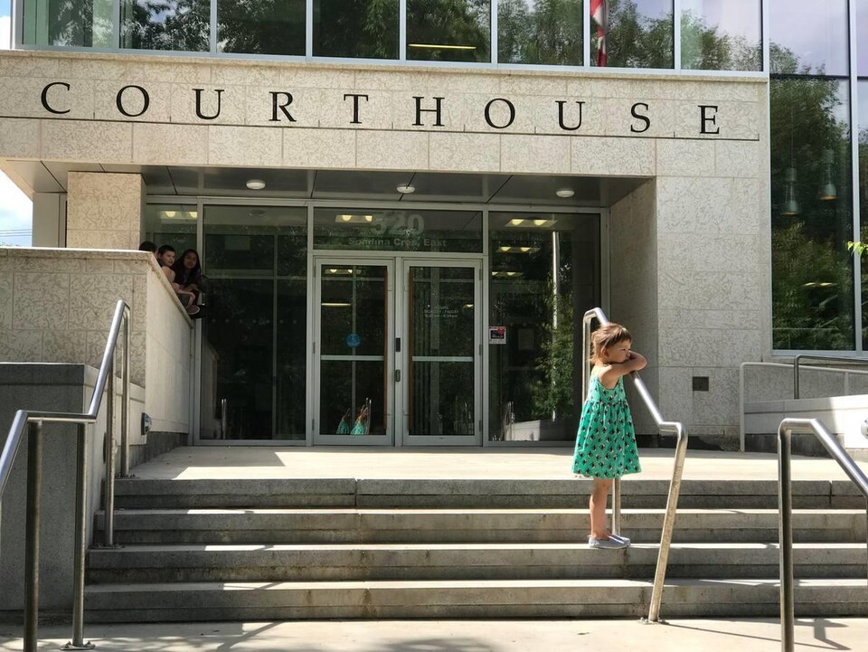 Une petite fille en robe verte, devant le palais de justince, s'appuie sur la rembarde de l'escalier extérieur.