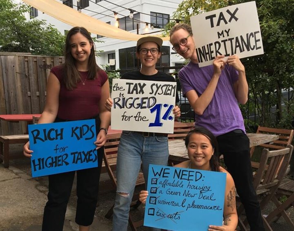 Des jeunes tiennent des pancartes sur lesquelles sont écrits en anglais divers slogans réclamant une plus grande taxation des riches.