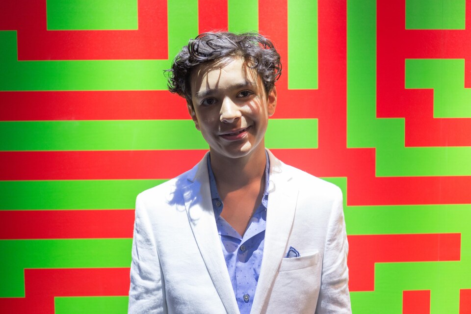 Une photo montrant Evan Sharma devant un mur composé de lignes verticales et horizontales vertes et rouges.