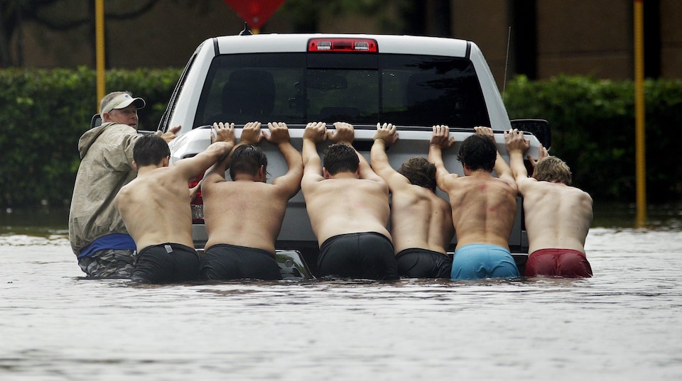 Des hommes poussent un camion bloqué sur une rue inondée de Houston, au Texas.