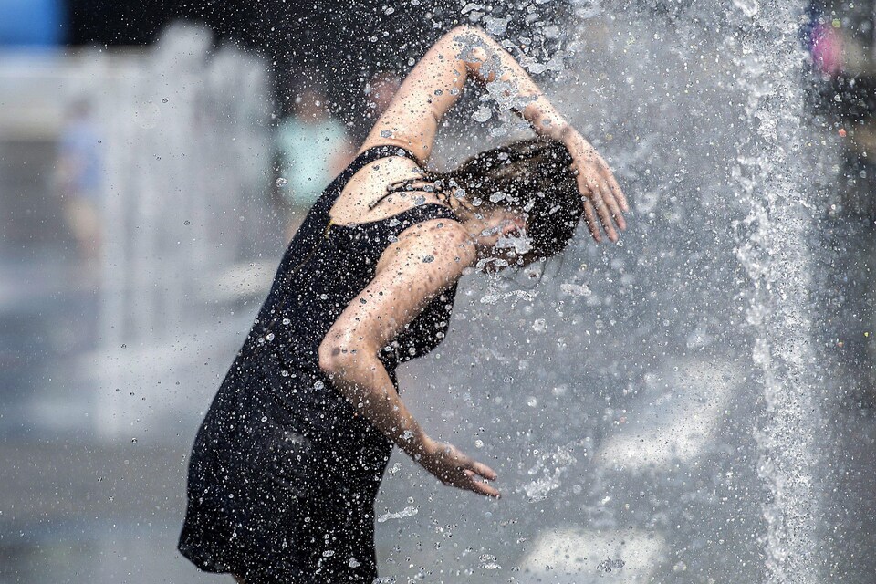 Une femme se rafraîchit dans une fontaine, à Montréal, pendant la canicule. 