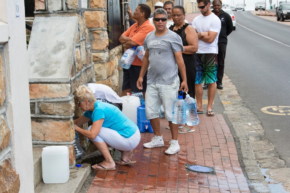 Des citoyens du Cap font la file sur le trottoir avec des bidons de plastique pour s'approvisionner en eau potable à l'aide d'un tuyau lié à une source souterraine.
