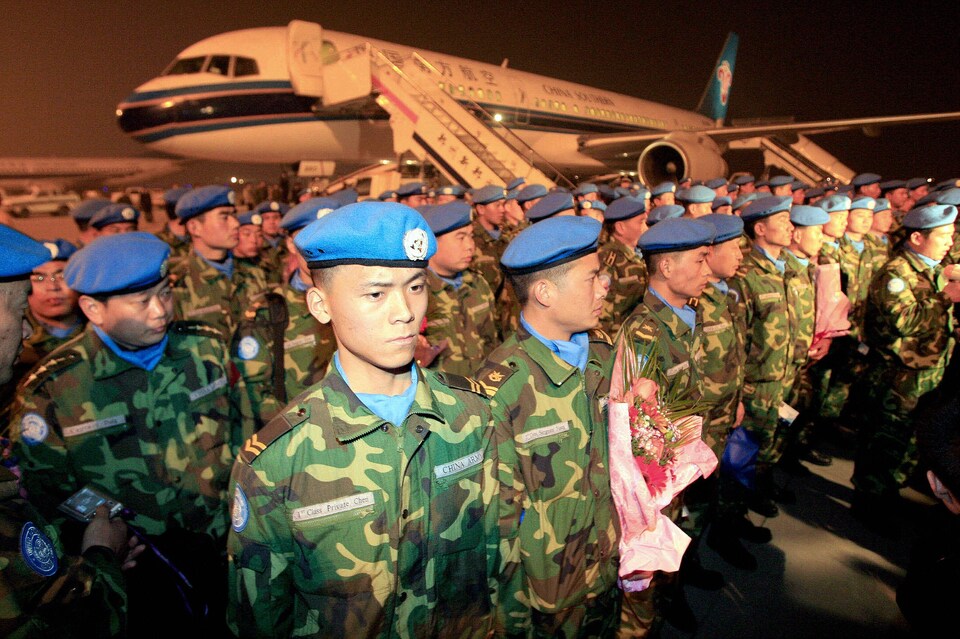 Des soldats coiffés d'un béret bleu attendent en formation devant un avion.
