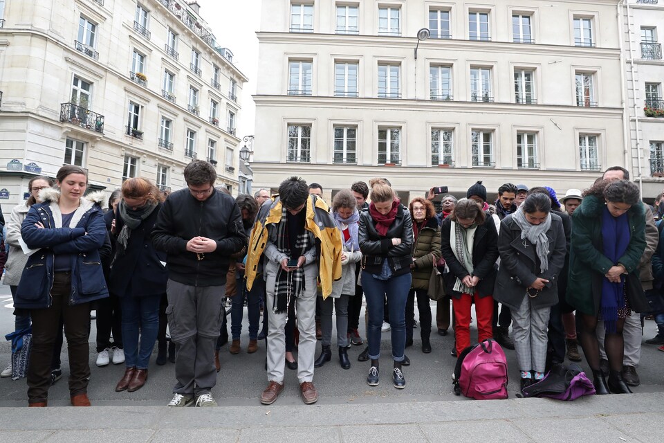 Des dizaines de personnes prient, la tête baissée, dans un espace public de Paris. 