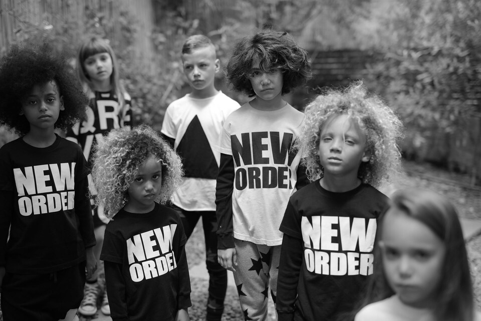 Plusieurs enfants de différents âges posent avec des vêtements sur lesquels est écrit New order.