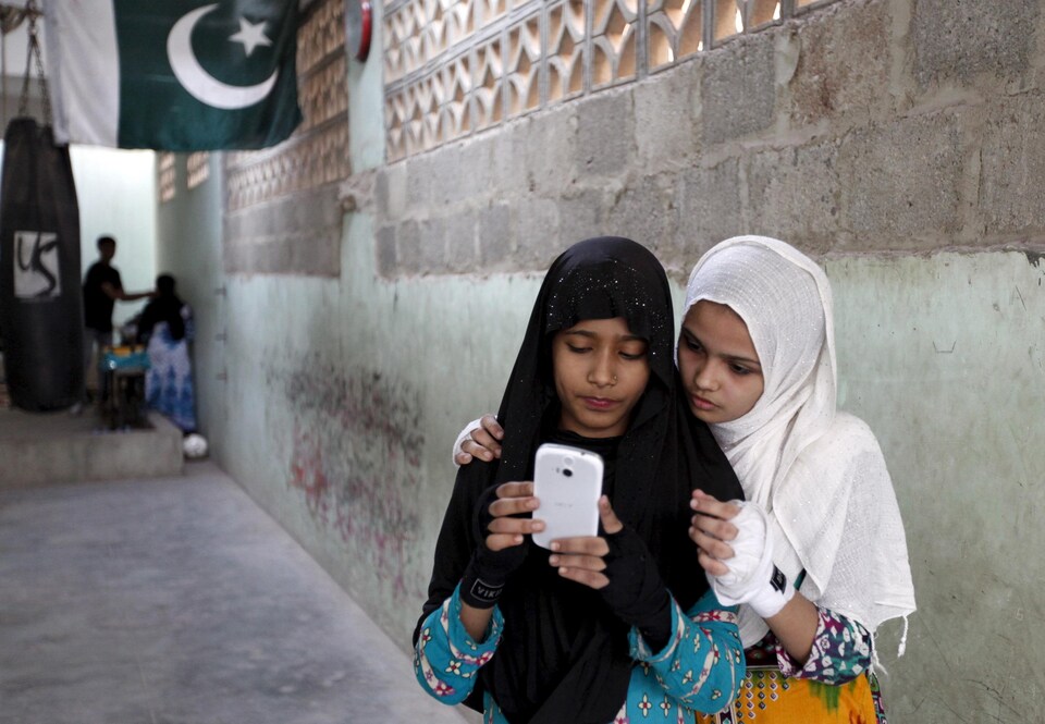 Deux jeunes Pakistanaises portant le voile regardent le même téléphone cellulaire blanc.