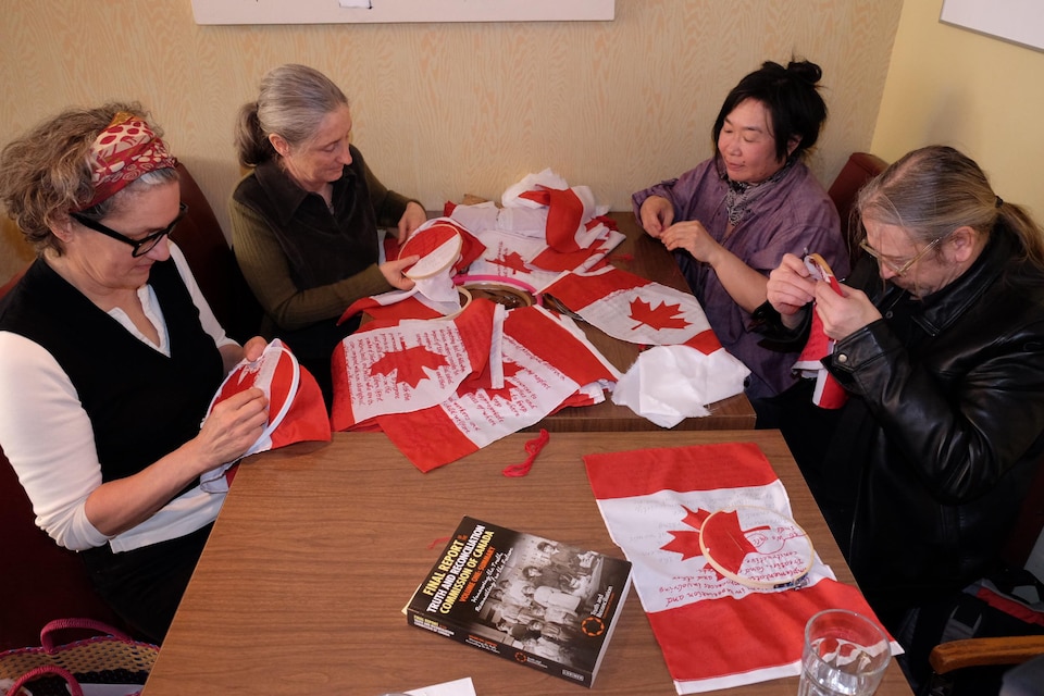 Un groupe de personnes brode des mots sur des drapeaux canadiens. 
