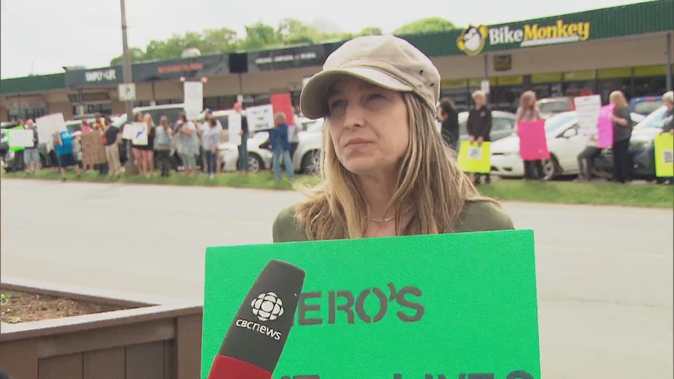 A woman holds a sign in front of dozens of protesters.