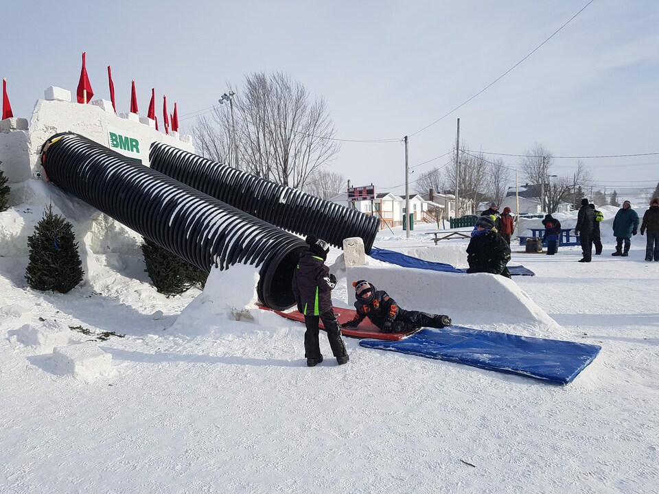 Des enfants glissent à travers de long tuyaux de plastique accrochés à un château de neige.