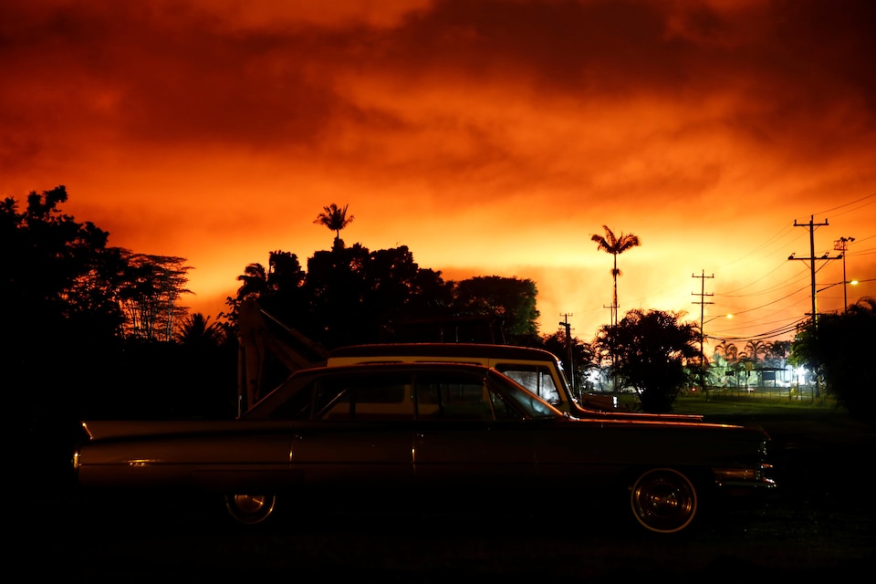 Deux voitures stationnées et quelques palmiers sous un ciel en feu