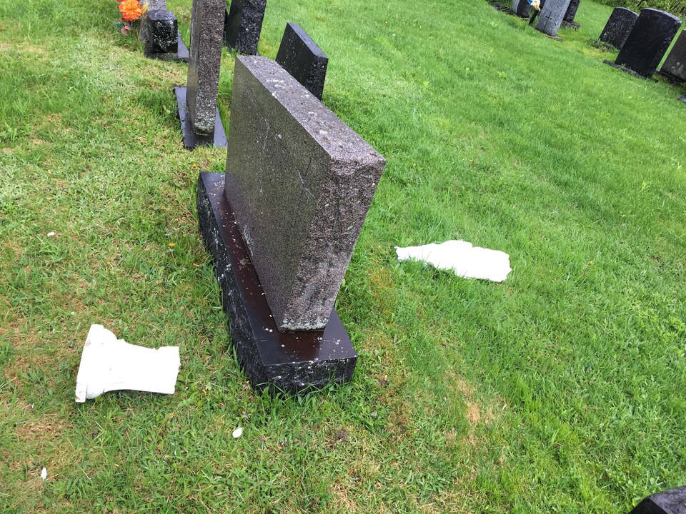 Une statue brisée devant une pierre tombale