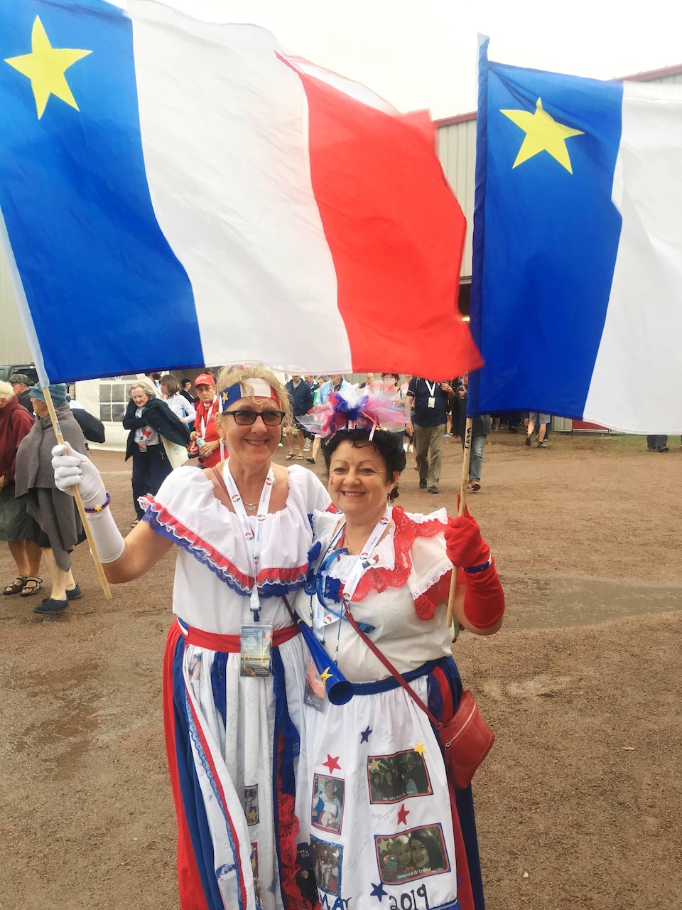 Deux femmes costumées brandissent des drapeaux de l'Acadie.