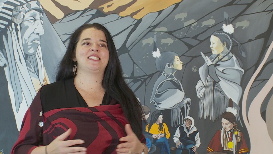 Une femme se tiens devant une murale.