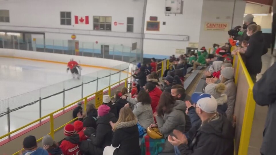 Les gens applaudissent le jeune hockeyeur qui patine devant eux dans l'aréna.