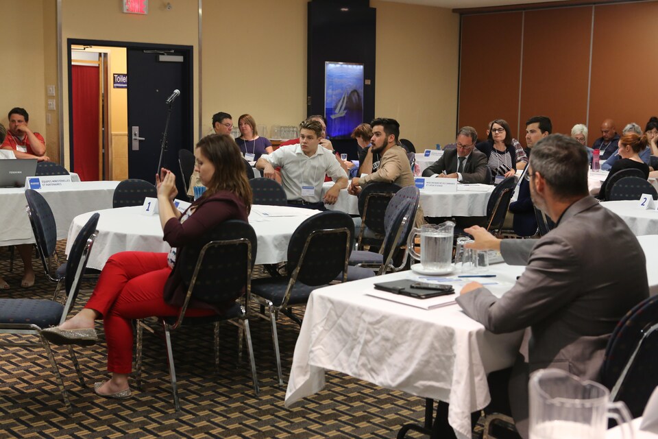 Des gens sont assis à des tables dans une salle de conférence.