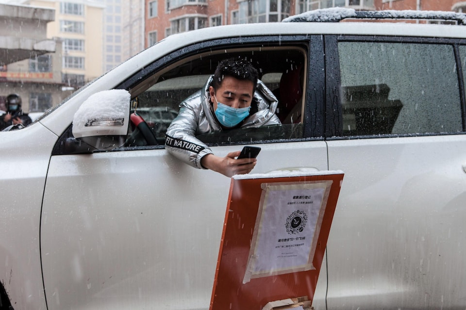 Un homme chinois scanne un code QR sur son téléphone en sortant son bras de sa voiture. Il porte un masque chirurgical.