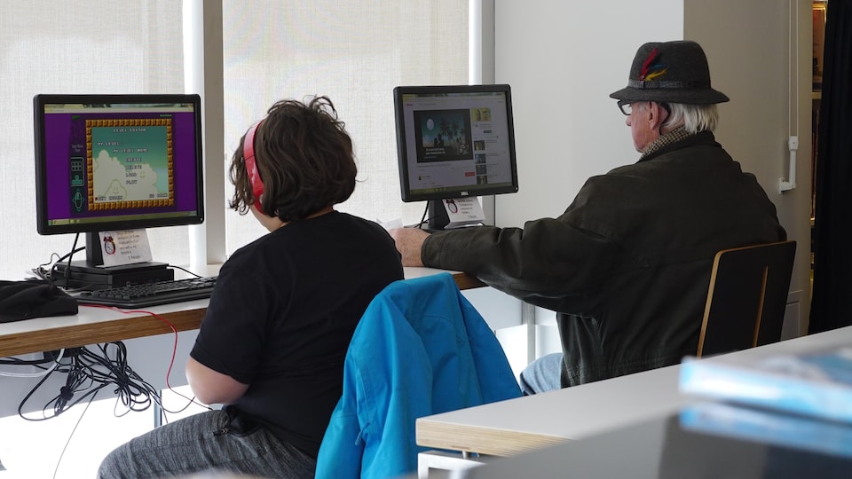 Un jeune homme devant un ordinateur en compagnie d'une personne âgée.
