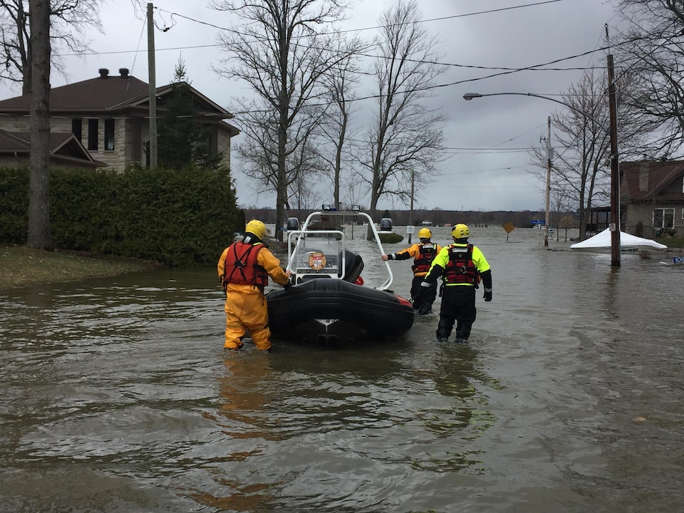 Des pompiers avec un bateau dans une rue inondée.