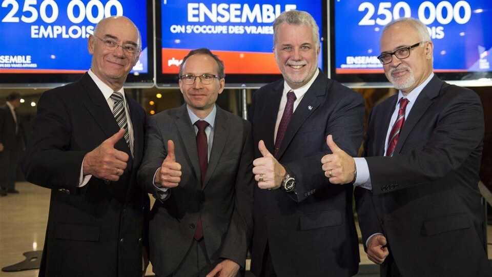 Jacques Daoust, Martin Coiteux, Philippe Couillard et Carlos Leitao lèvent leur pouce en l'air devant des slogans électoraux.
