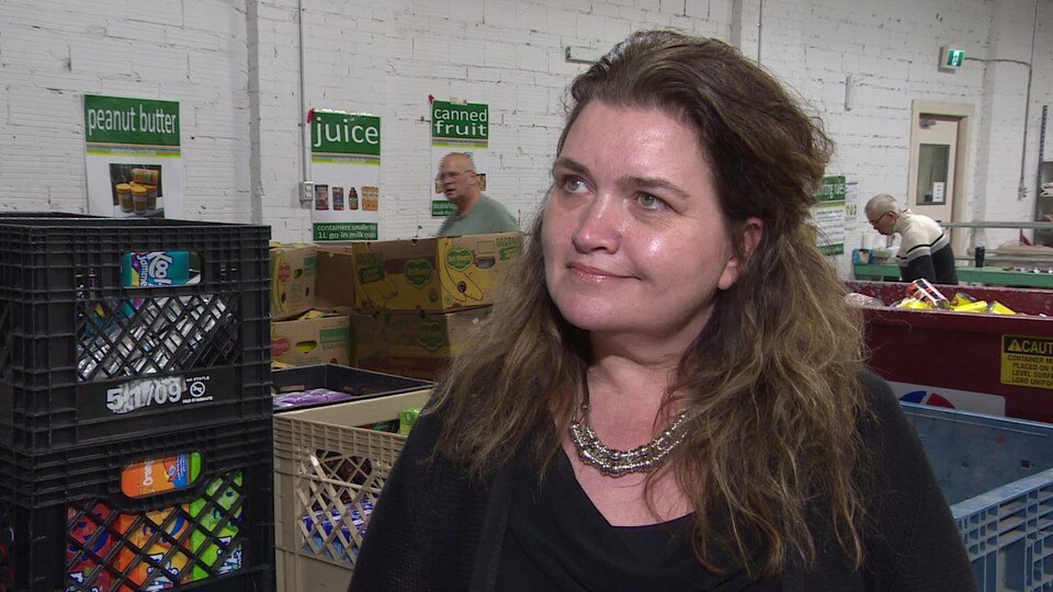 Deborah Hamp écoute une question du reporter devant des boîtes remplies de denrées alimentaires.