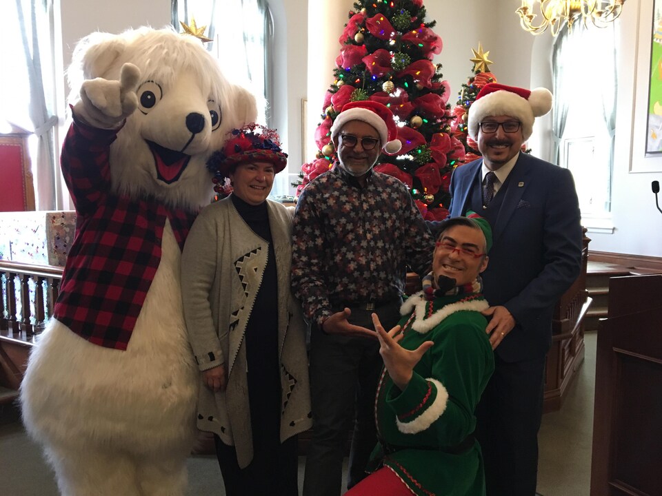 Les quatre intervenants sourient devant un arbre de Noël en compagnie d'une mascotte d'ours polaire. 