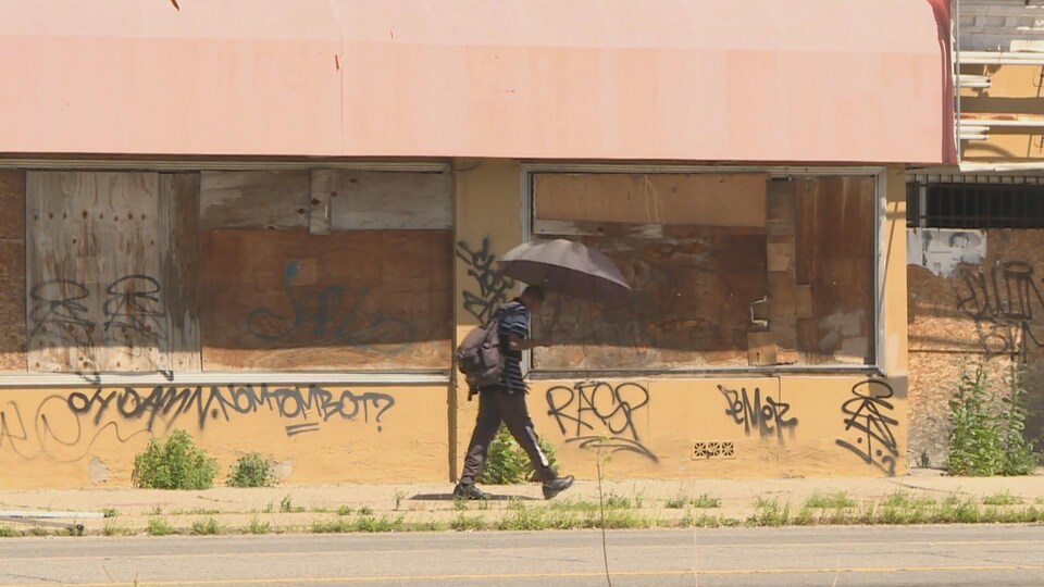 Un homme marche avec un parapluie noir devant un mur de graffitis.