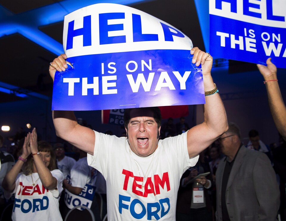 Un partisan de Doug Ford tient une affiche bleue dans ses mains.
