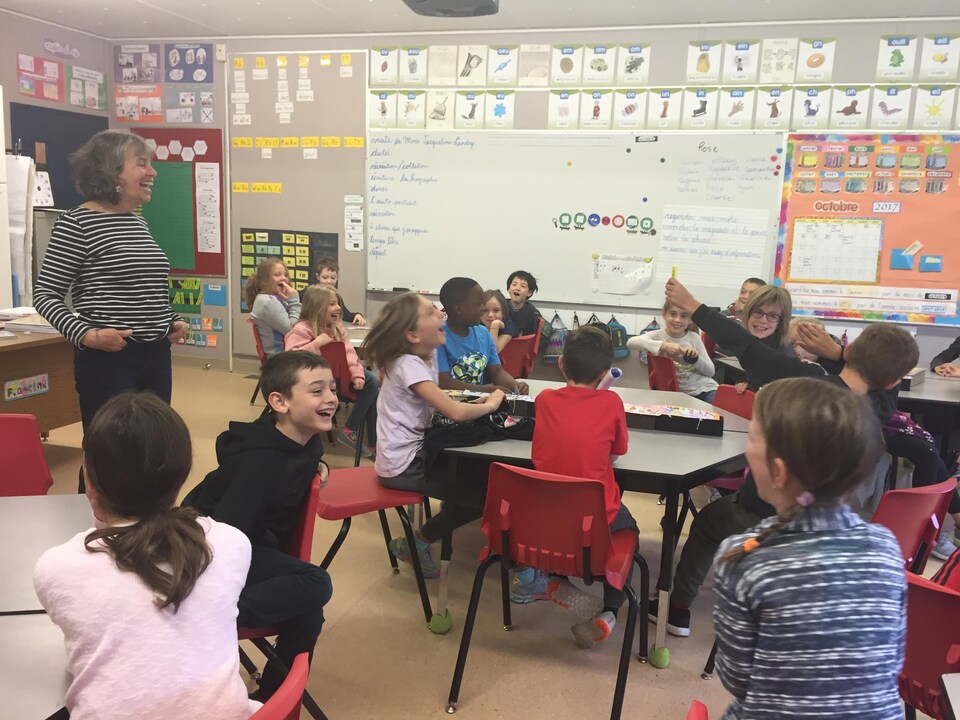 Des élèves de 3e année rient et participent à une activité en français dans leur salle de classe en s'amusant.