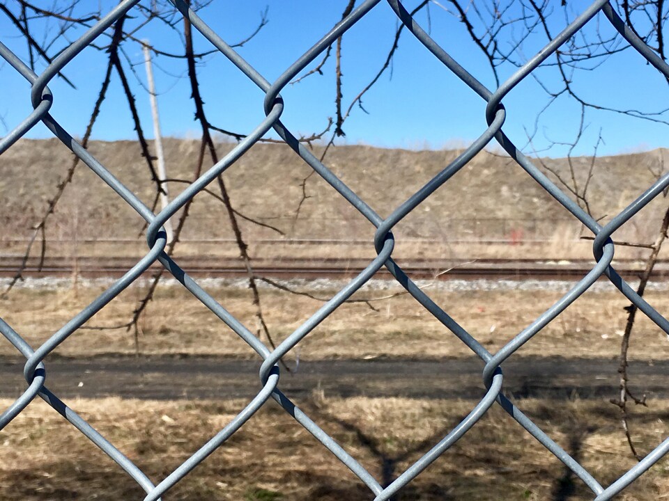 Le terrain contaminé vu de l'autre côté d'une clôture de broche.