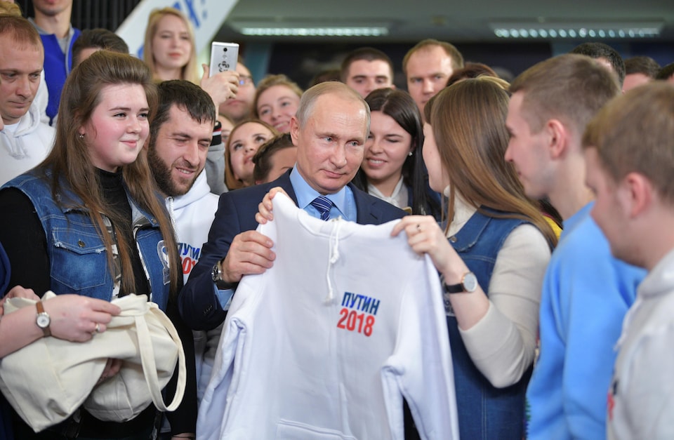 Une jeune femme offre un chandail au président Poutine. Ils sont entourés d'une vingtaine de jeunes qui sourient.