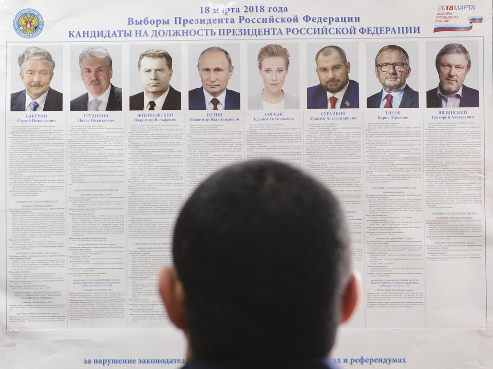 Un homme regarde une affiche sur laquelle apparaissent les huit candidats à l'élection.