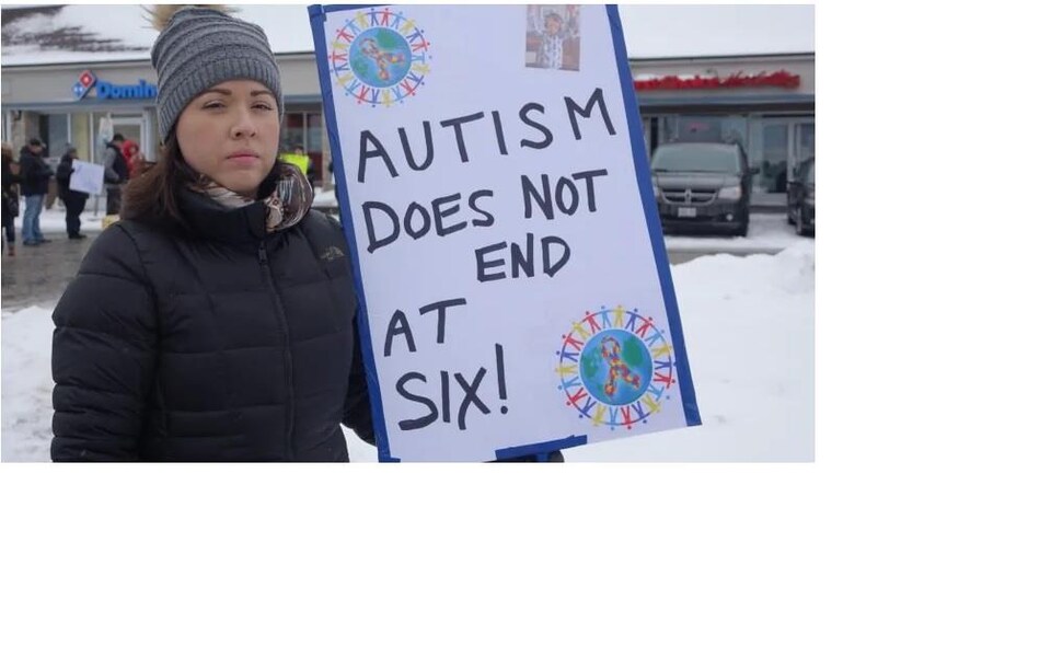 Emily Sheridan à l'extérieur. Elle tient une pancarte sur laquelle on peut lire « Autism Does Not End At Six! »